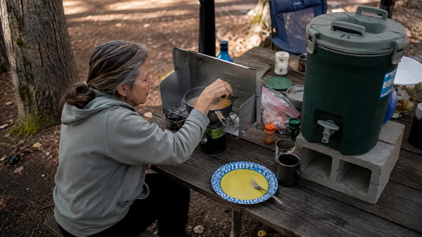 A cramped picnic table at a small campsite with the water dispenser taking up nearly a third of the surface, leaving little room for a camp stove and plates