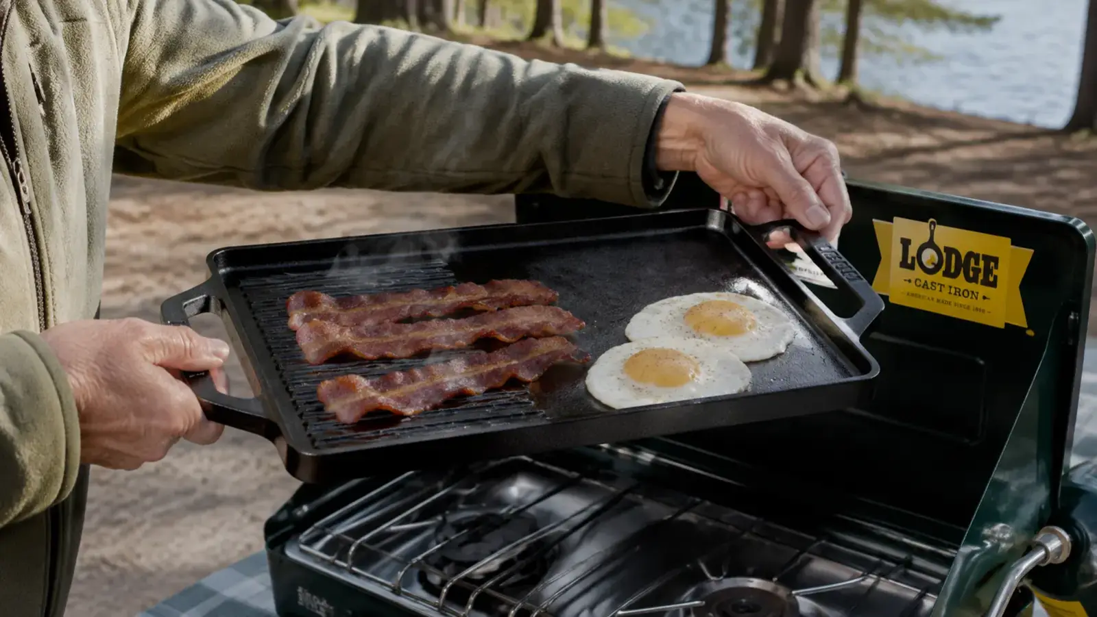 An older woman's hands lifting the Lodge reversible cast iron griddle off a two-burner camp stove after cooking breakfast