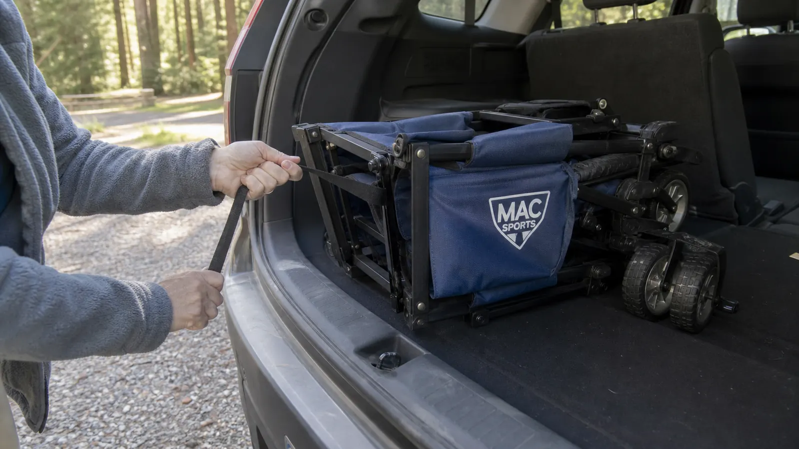 Close-up of a pair of hands folding a blue collapsible utility wagon flat before lifting it into the back of an SUV alone