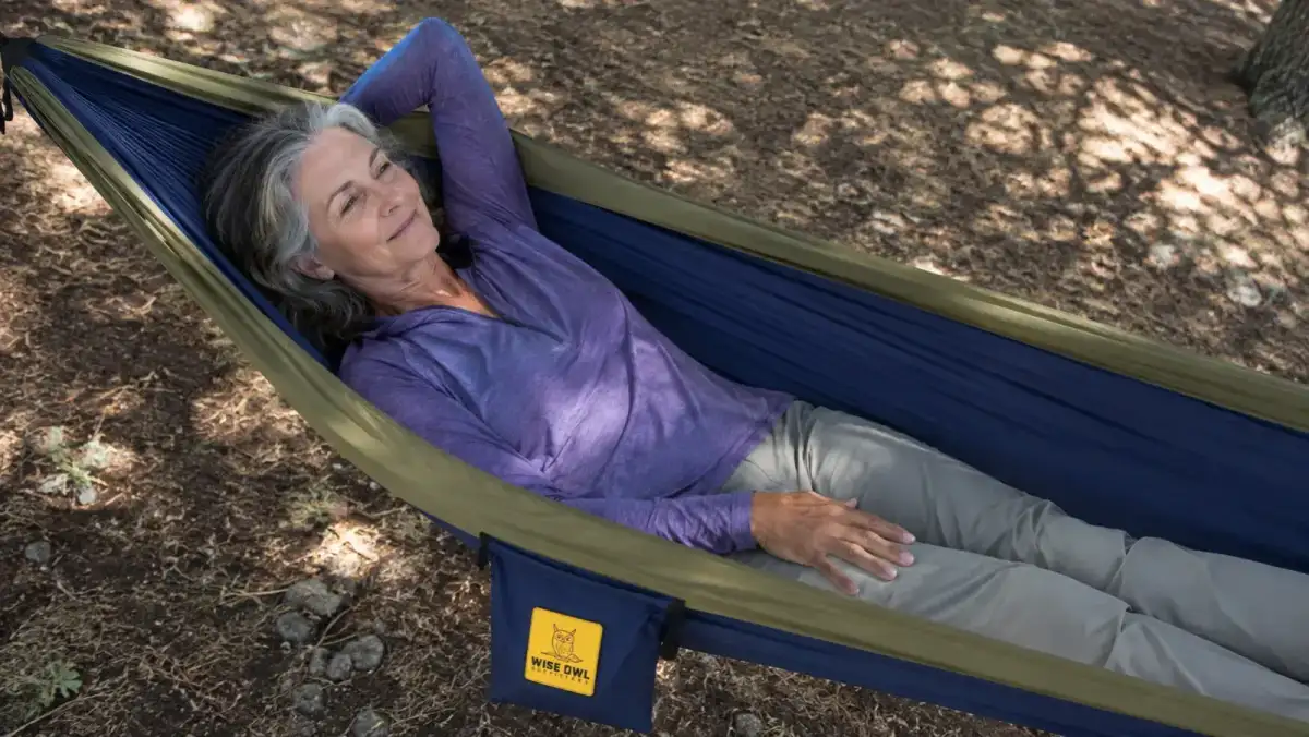 A woman lying diagonally across a camping hammock instead of straight down the center to avoid shoulder squeeze